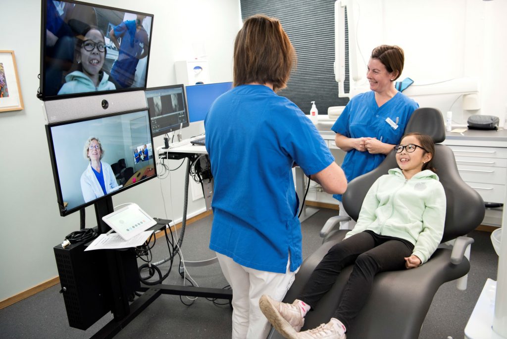 Ella, 9 år, får distanskonsultation av ortodontispecialisten Boel Gunnarsson. Bredvid Ella syns tandläkaren Rodica Dragan och klinikkoordinatorn Annie Molarin.
