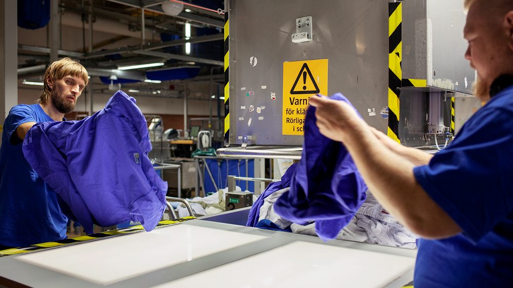 Bild på två personer som står och hanterar blå sjukhuskläder.