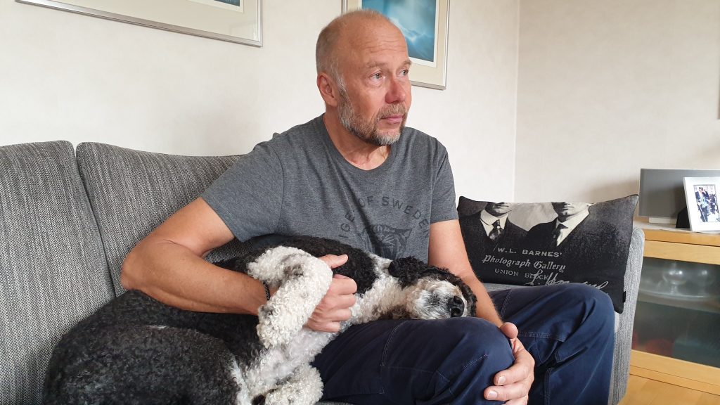 Bil på Mats som sitter i sin soffa med en hund som ligger i hans knä.