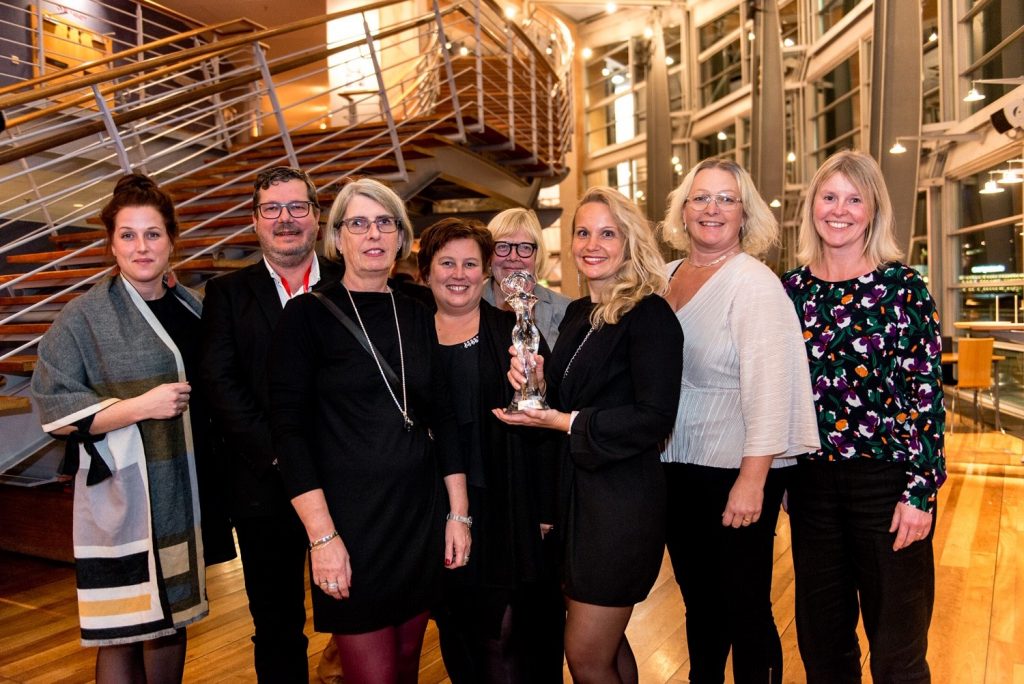 Projektledare Maria Klingborg med prisstatyetten tillsammans med från vänster: Maria Karlsson, vårdutvecklare Samverkande sjukvård, Markus Lawson, teknisk specialist ambulansen, Lena Olsson, medicinskt ansvarig sjuksköterska Strömstad och Tanum, Helene Larsson, enhetschef Mobila vårdteamet i Uddevalla och samordnare för Samverkande sjukvård Marianne Laiberg, regionutvecklare koncernkontoret, Angelica Uddén och Yvonne Lussenburg, sjuksköterskor hemsjukvården i Bengtsfors.