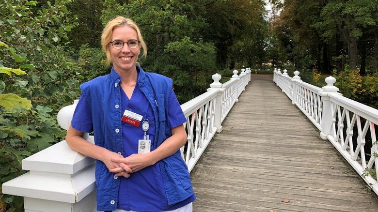 Bild på Susanne som står på en gångbro, lutar sig mot ett räcke, klädd i blå läkarklädsel.