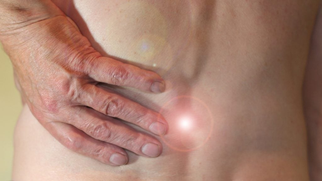 Bild på en mans hand som tar sig om ryggen, det ser ut som han har ont.