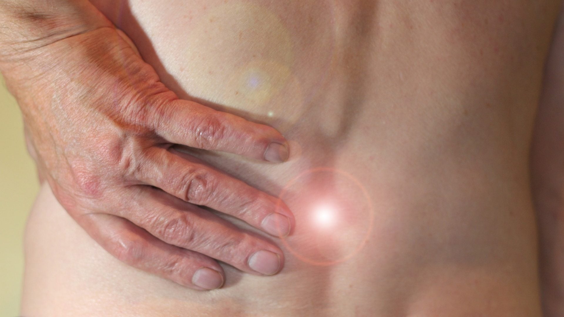 Bild på en mans hand som tar sig om ryggen, det ser ut som han har ont.