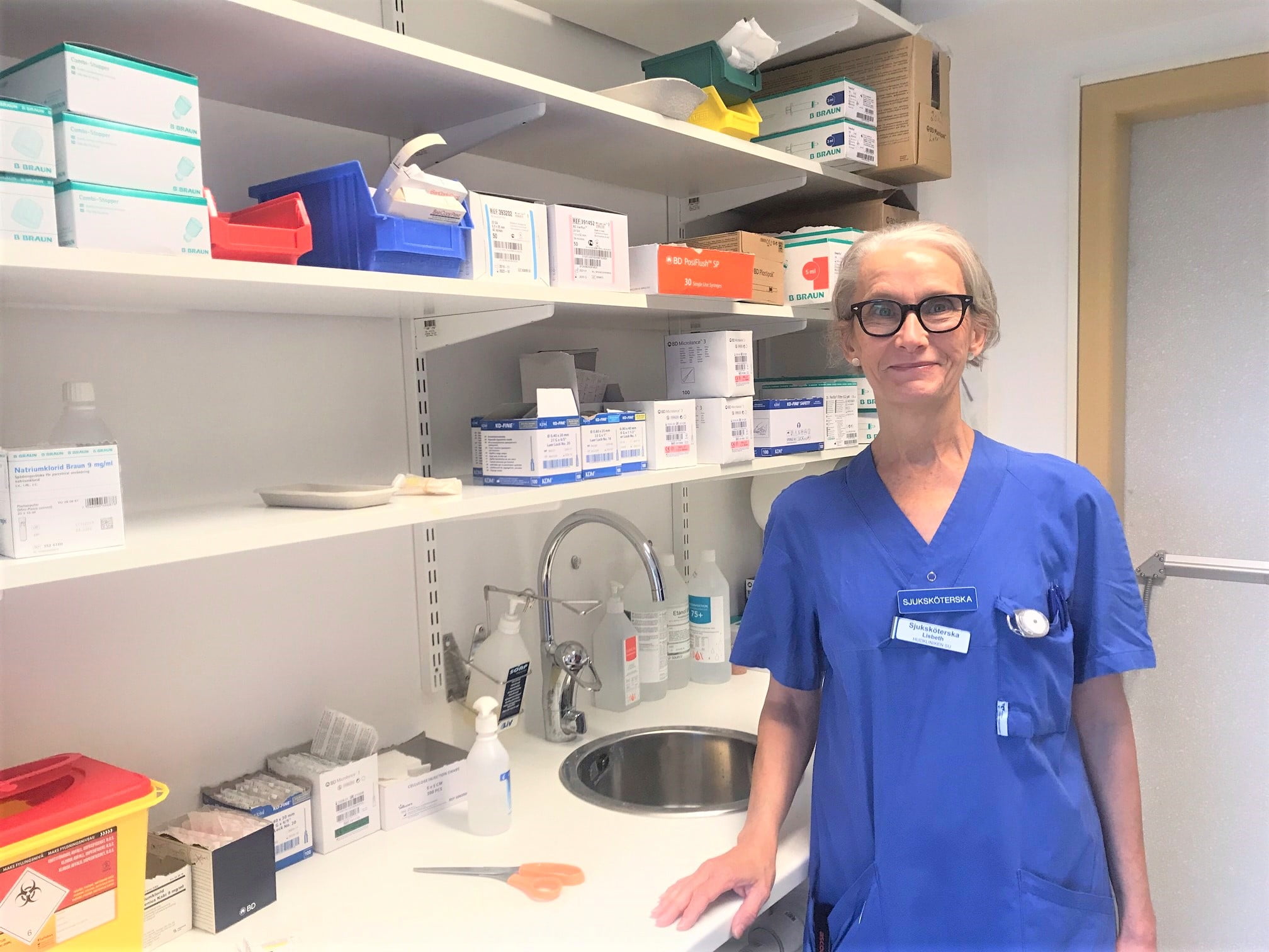 Lisbeth Wallen, sjuksköterska står i arbetskläder vid en bänk där det finns medicinsk utrustning.