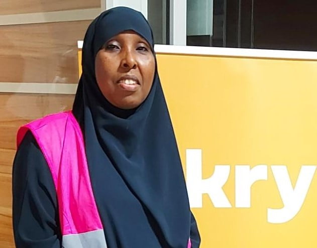 Saido Mohamed jobbar som kulturtolk i Göteborg. Hon står i rosa reflexväst vid en skylt som det står Kry på.