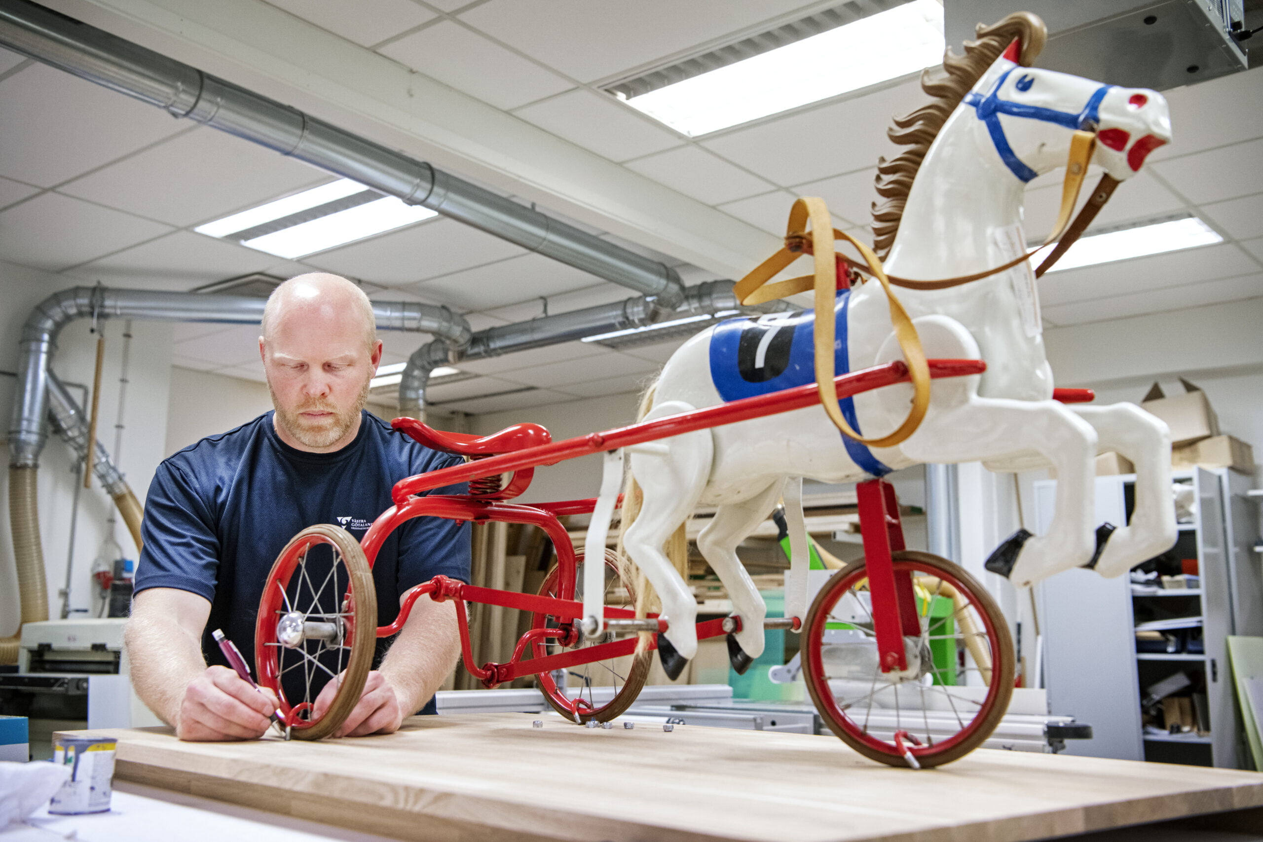 Hans Persson monterar leksakshästen på en låg sockel av ek. Hästen ska till en barn- och ungdomspsykiatrisk mottagning i Borås. Den ska tåla att klättras på, men måste monteras fast ordentligt så det inte går att köra iväg med den. Foto: Kent Eng.