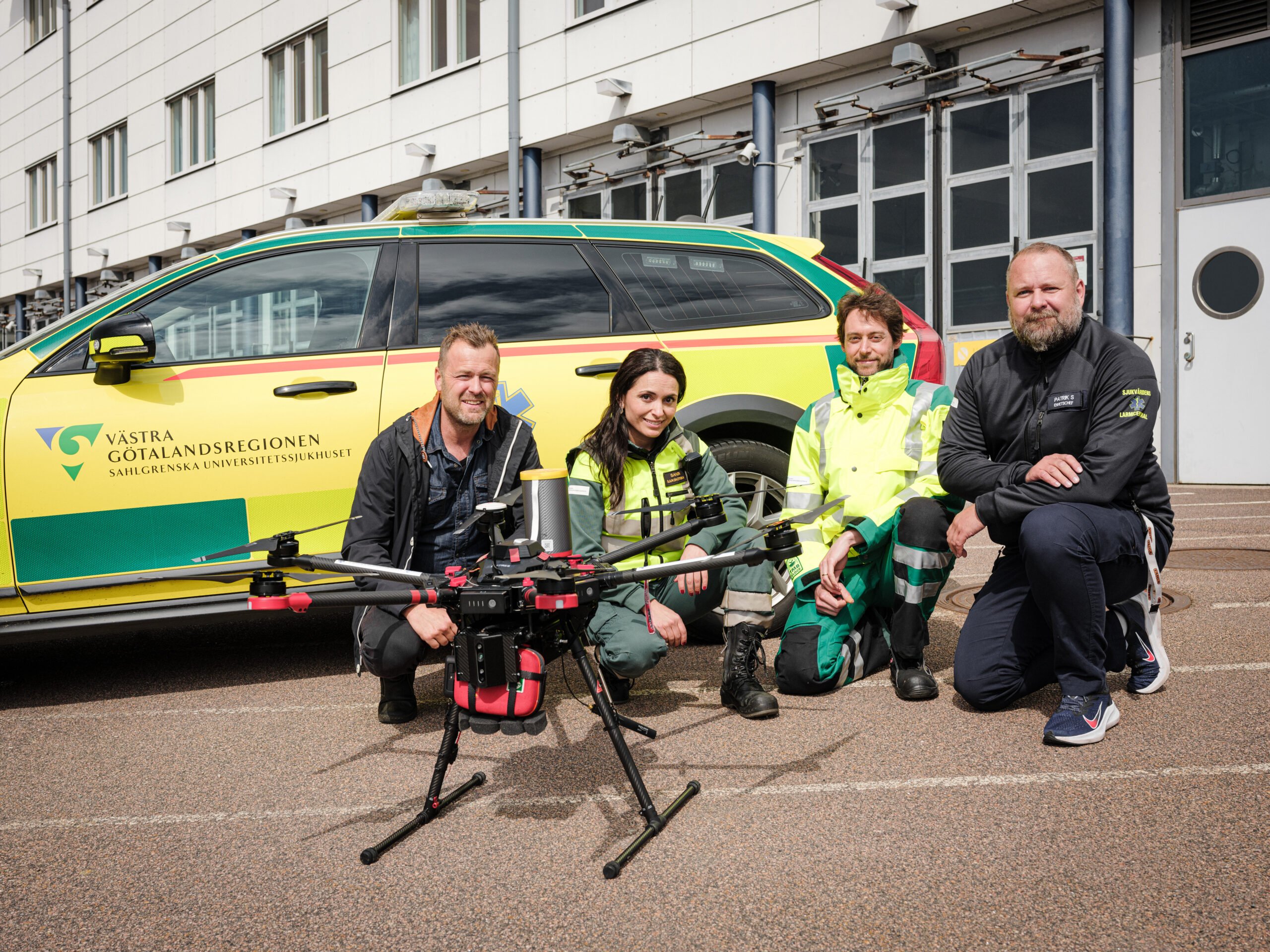Sandra Merino – sjuksköterska, och Alexander Haner – akutläkare. Båda anställda på ambulansen SU. Magnus Kristiansson, innovationsledare på Innovationsplattformen, Patrik Andersson Segerfelt, enhetschef Sjukvårdens Larmcentral, VGR. Sitter på huk framför en ambulans och har drönaren på marken framför sig.