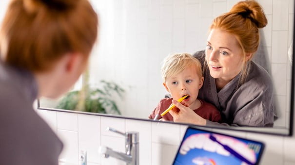 En mamma och ett barn borstar tänderna tillsammans.