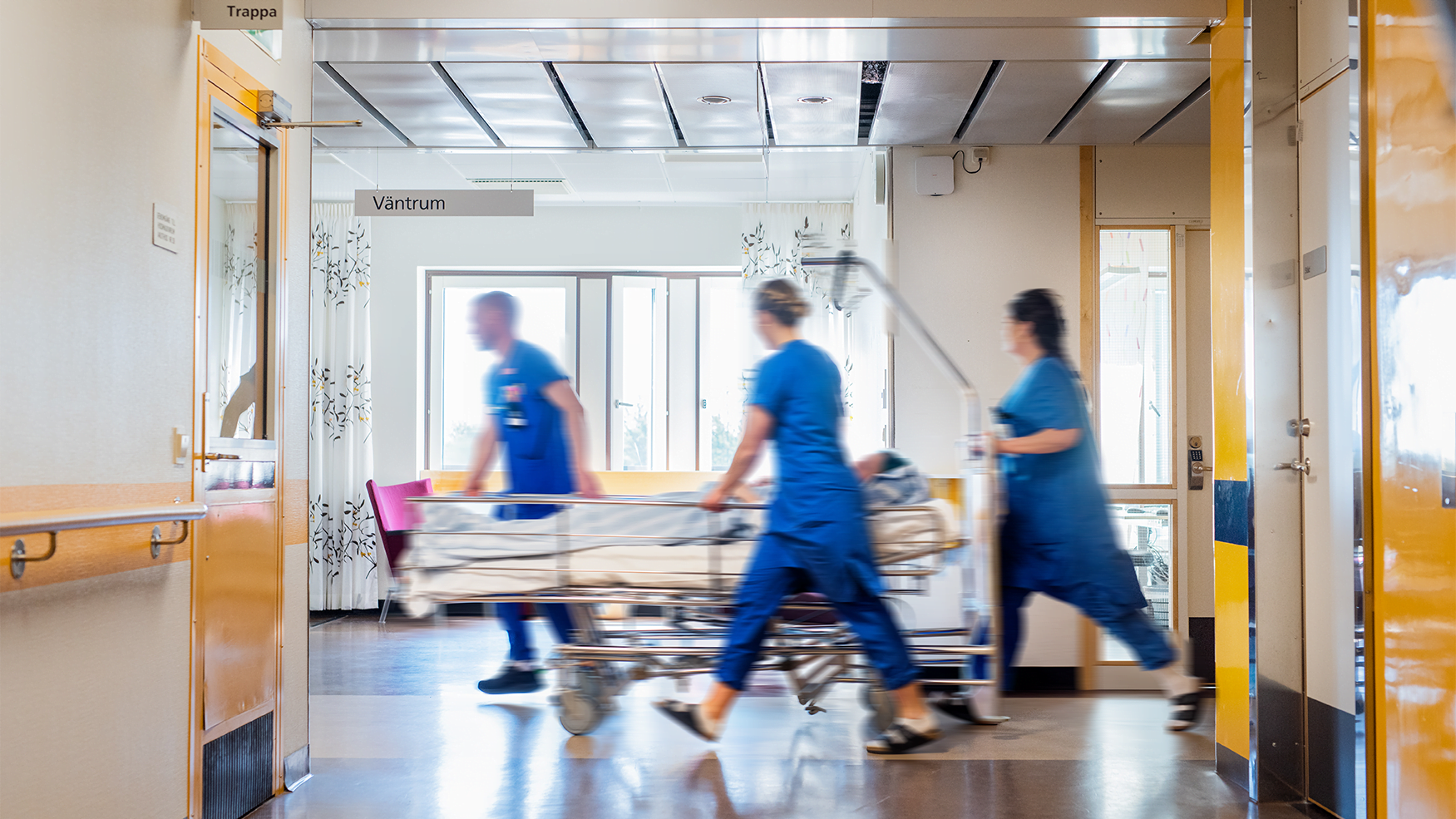 Vårdpersonal går snabbt med en sjuksäng genom en korridor