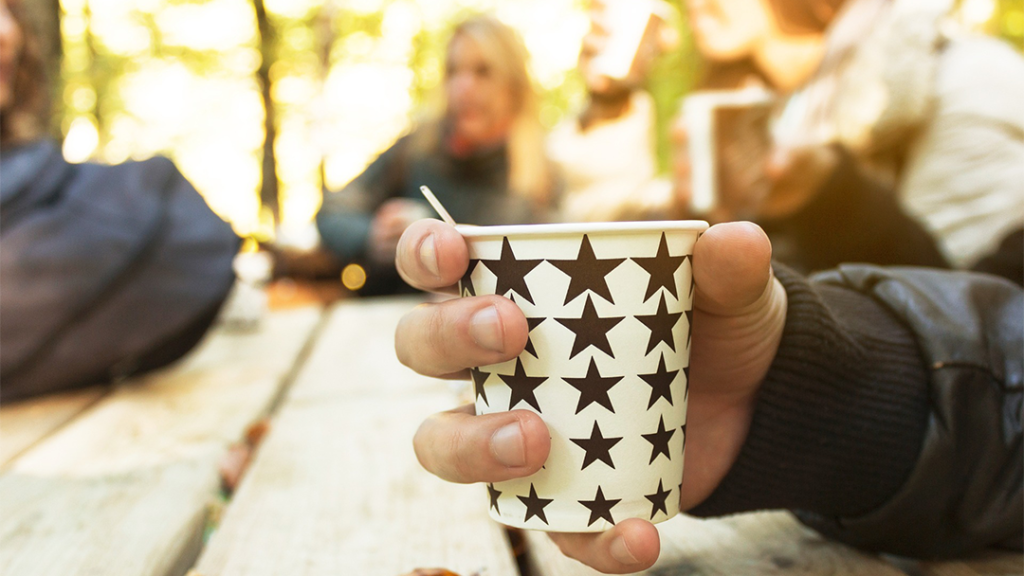 En hand håller i en kaffemugg. Bilden föreställer en fikasituation.