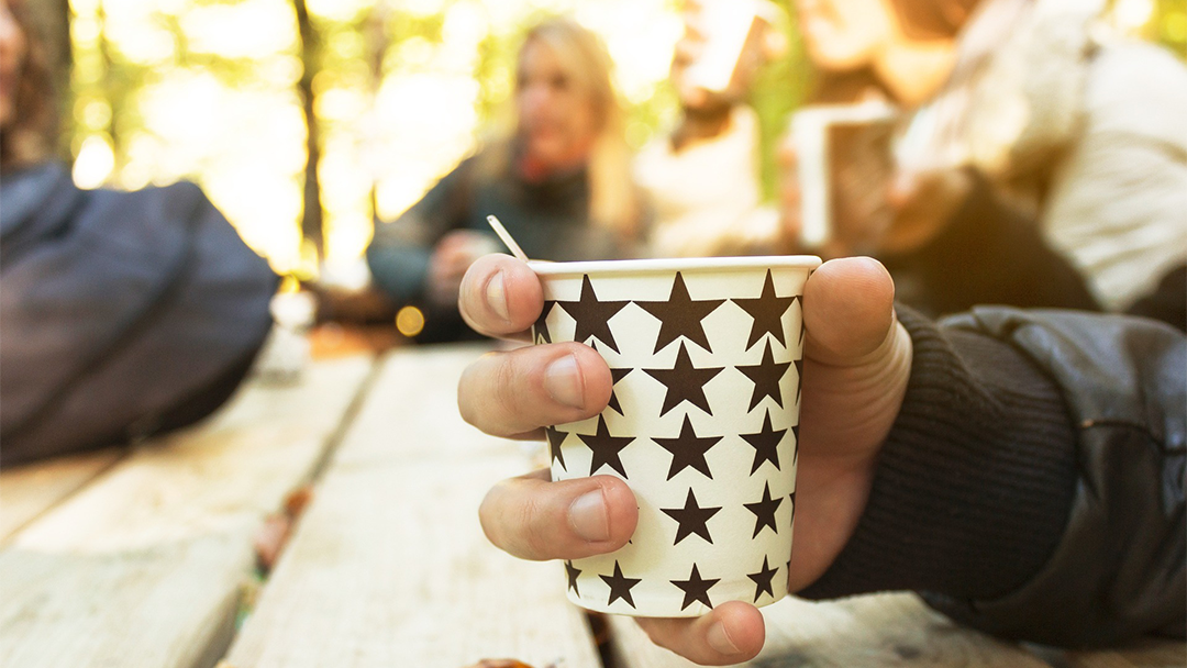 En hand håller i en kaffemugg. Bilden föreställer en fikasituation.